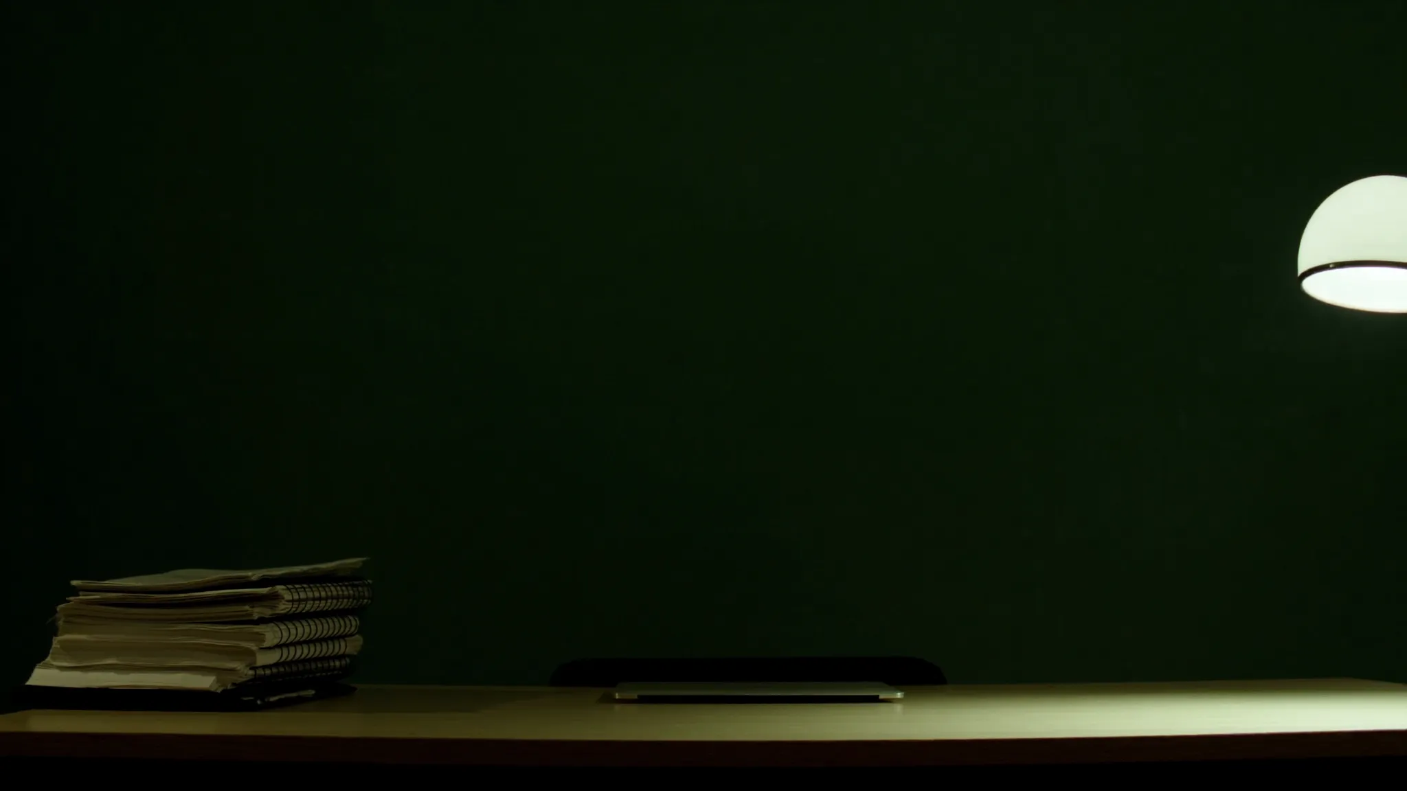 An empty desk in a dark green room, papers stacked with no readable marks